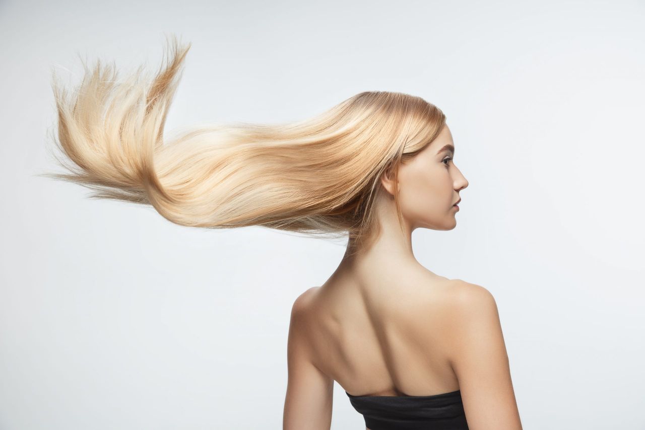 Beautiful model with long smooth, flying blonde hair isolated on white studio background. Young caucasian model with well-kept skin and hair blowing on air. Concept of salon care, beauty, fashion.