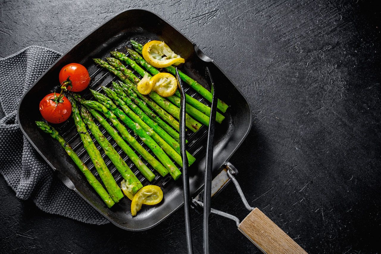 Tasty appetizing grilled asparagus with spices on grill pan on dark background. View from above with copy space.