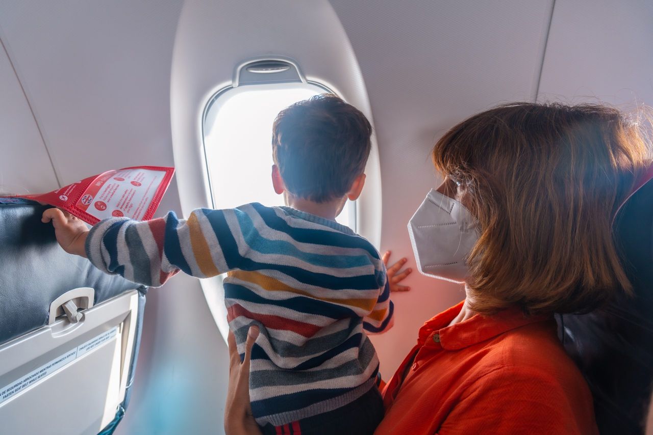 Boy traveling by plane on vacation with his mother looking out the window, watching the landing