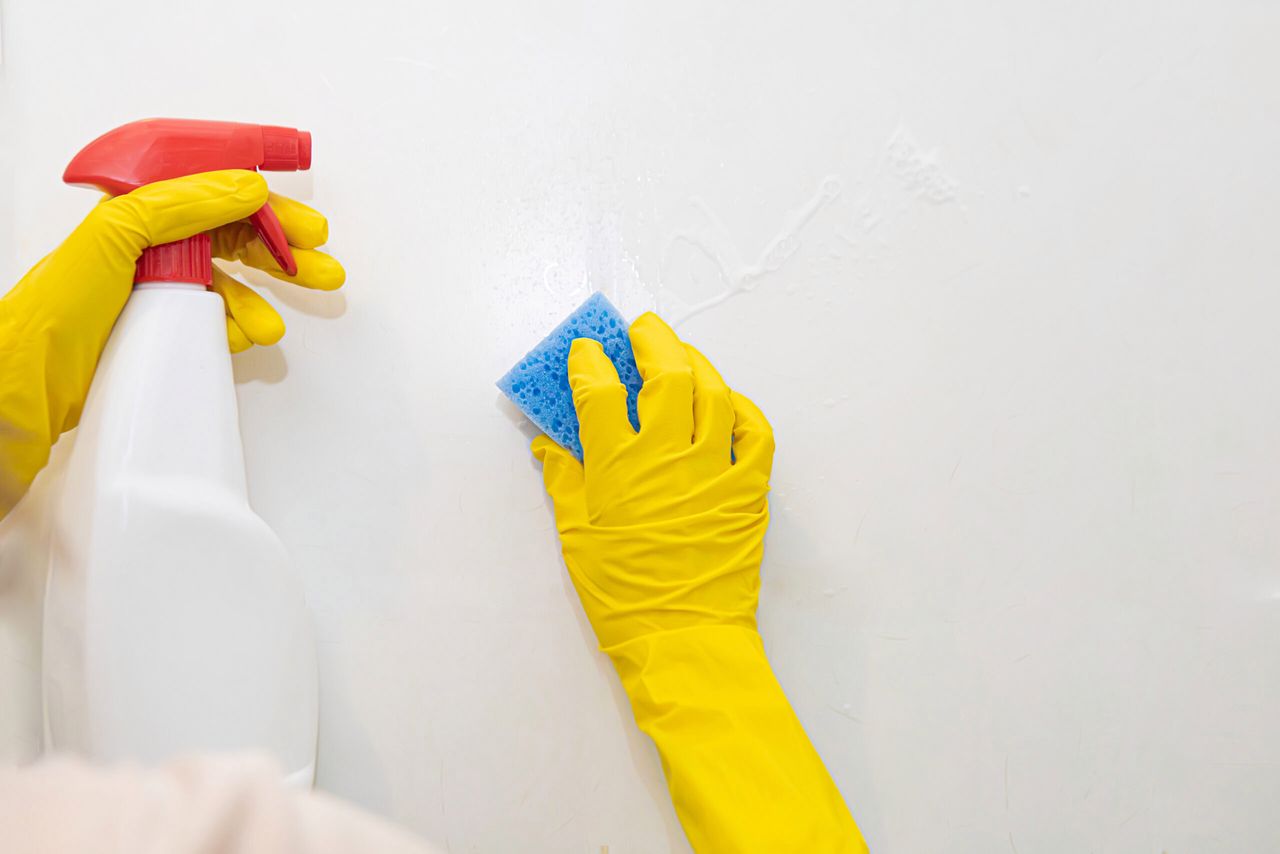 Hands in yellow rubber gloves washing the tiles in the bathroom. Close-up.