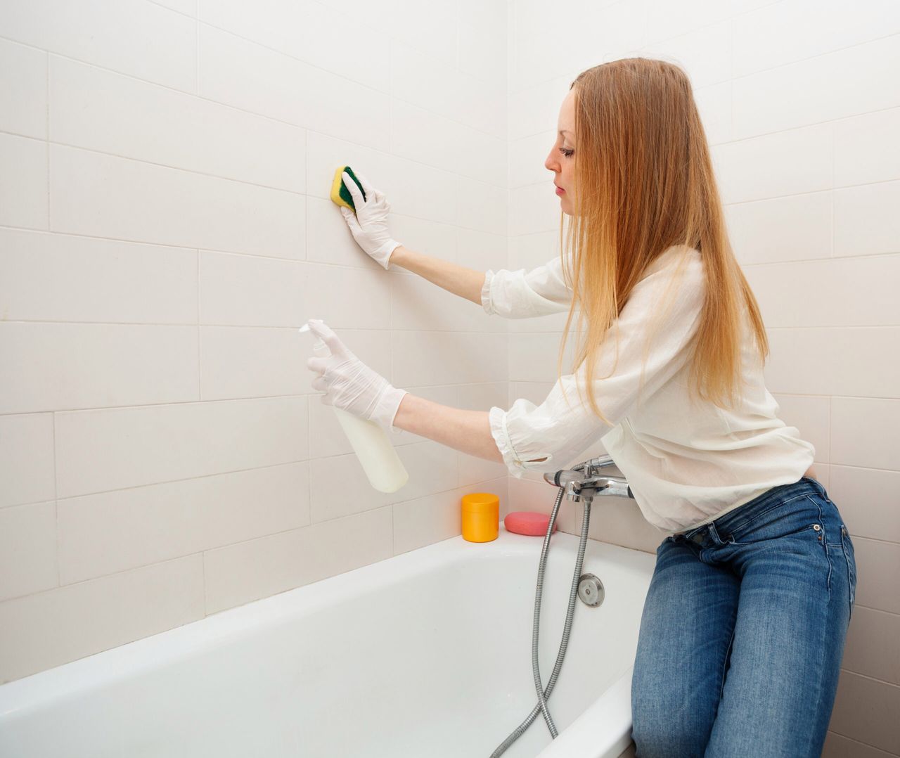 long-haired woman cleaning tile with sponge in bathroom at home