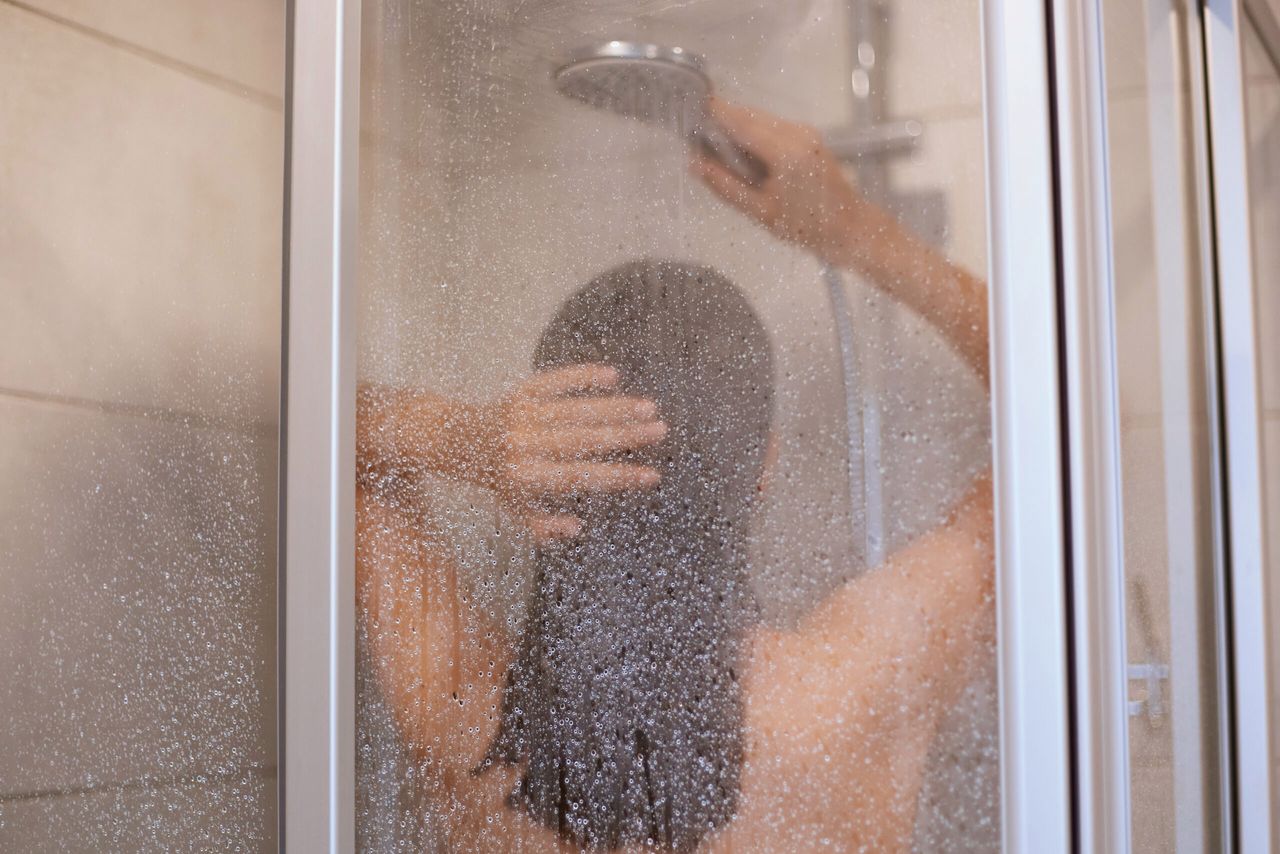 Enjoying a shower. Back view of beautiful young slim shirtless woman taking shower, washing hair in bathroom, hygiene, healthy and beauty, indoor shot.