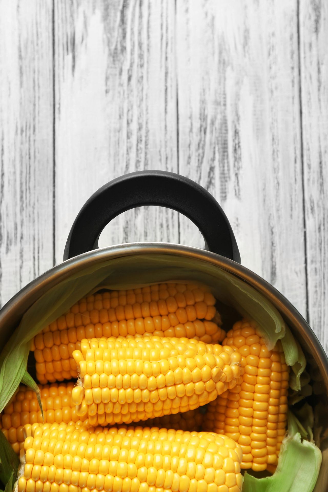 Tasty boiled corncobs in saucepan on wooden table