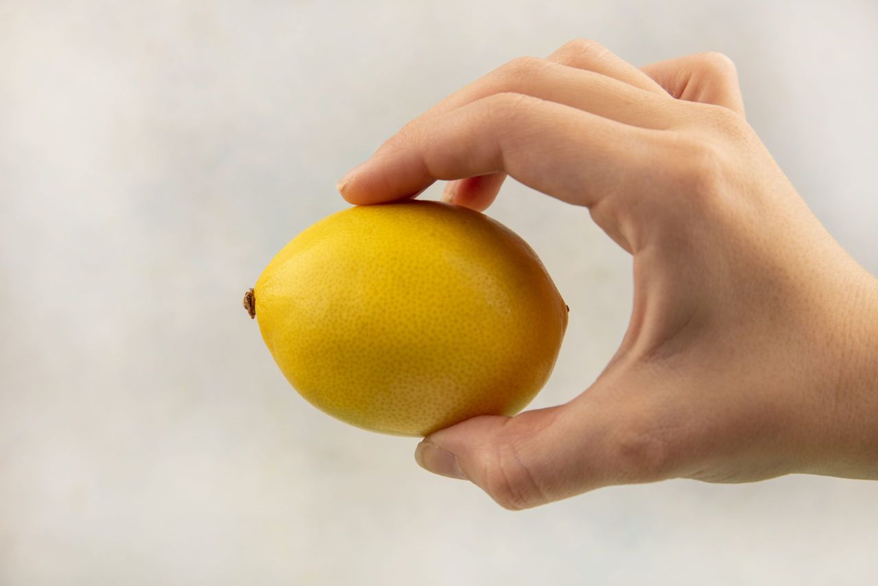 top view of female hand holding citrus fruit lemon on a white background