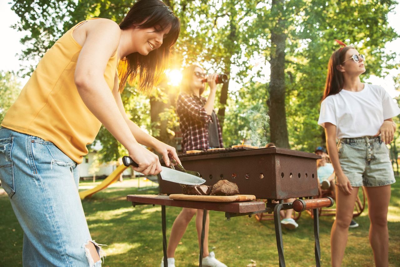 Group of happy friends having beer and barbecue party at sunny day. Resting together outdoor in a forest glade or backyard. Celebrating and relaxing, laughting. Summer lifestyle, friendship concept.