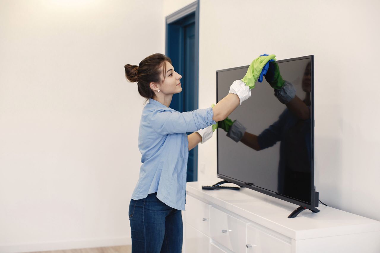 Housewife woking at home. Lady in a blue shirt. Woman clean TV.