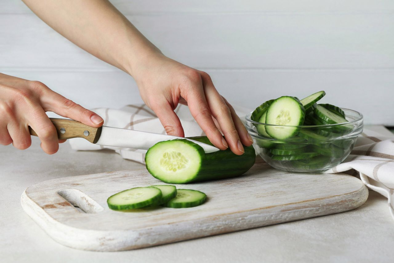 Woman cuts a cucumber on wooden board