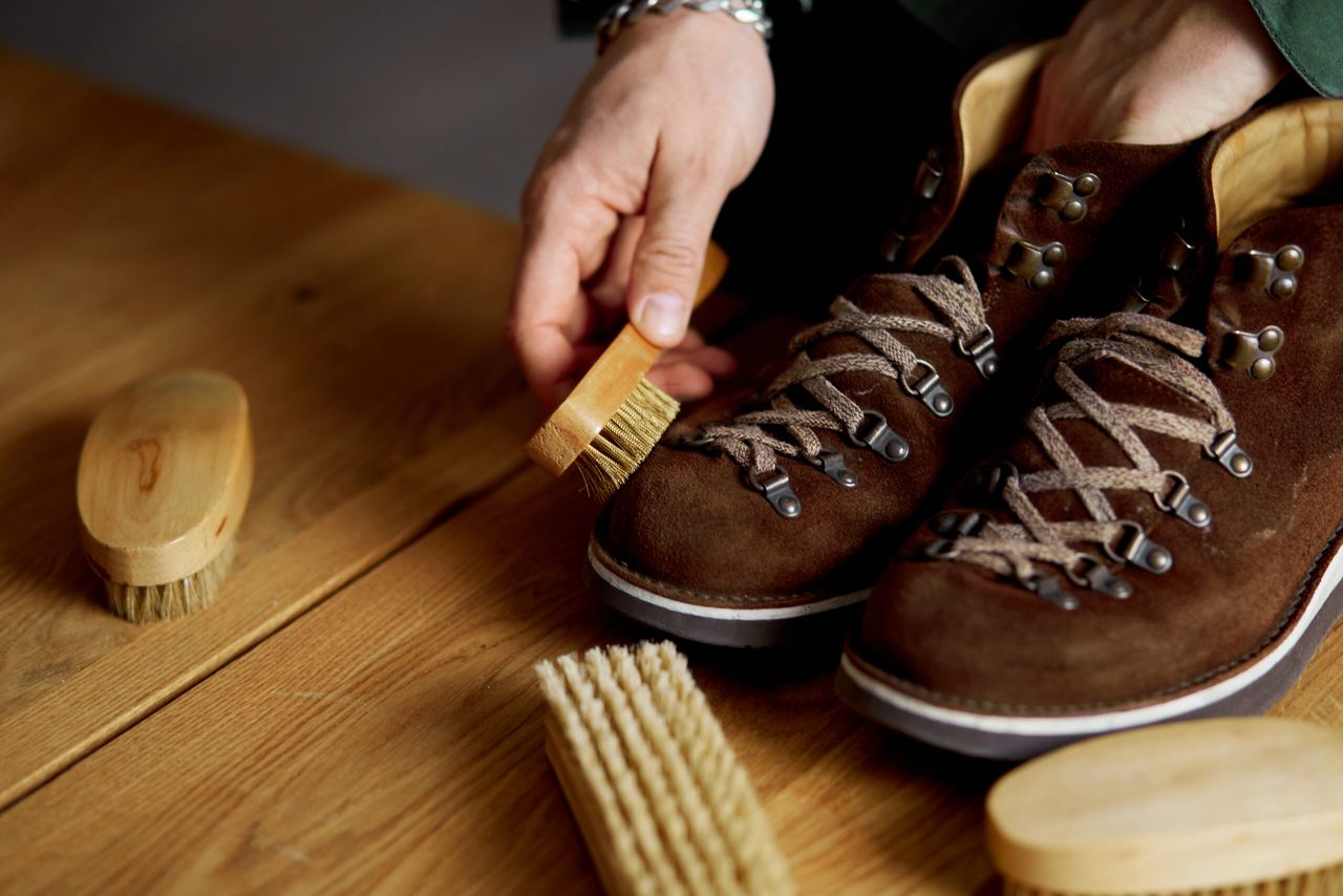 Man's hand clean suede shoes, boots with a brush on wooden background. Footwear maintenance captured, copy space, for text.