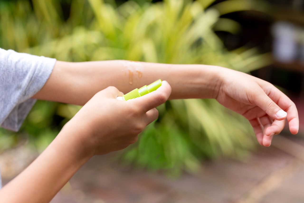 Young boy spraying insect repellent against mosquitos bites on his arm in the garden