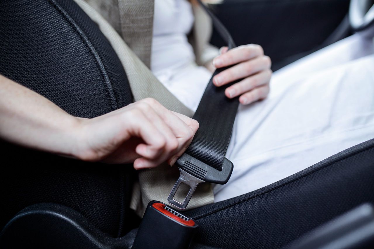cropped view of woman fastening safety belt while sitting in car on blurred foreground. Cut view of young woman's hands locking seat belt in car. Sitting alone. Close up