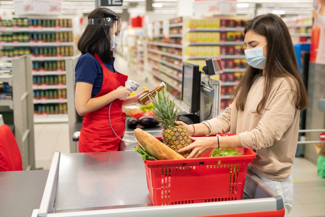 Supermarket cashier and customer following personal protection rules during coronavirus quarantine days, wearing masks