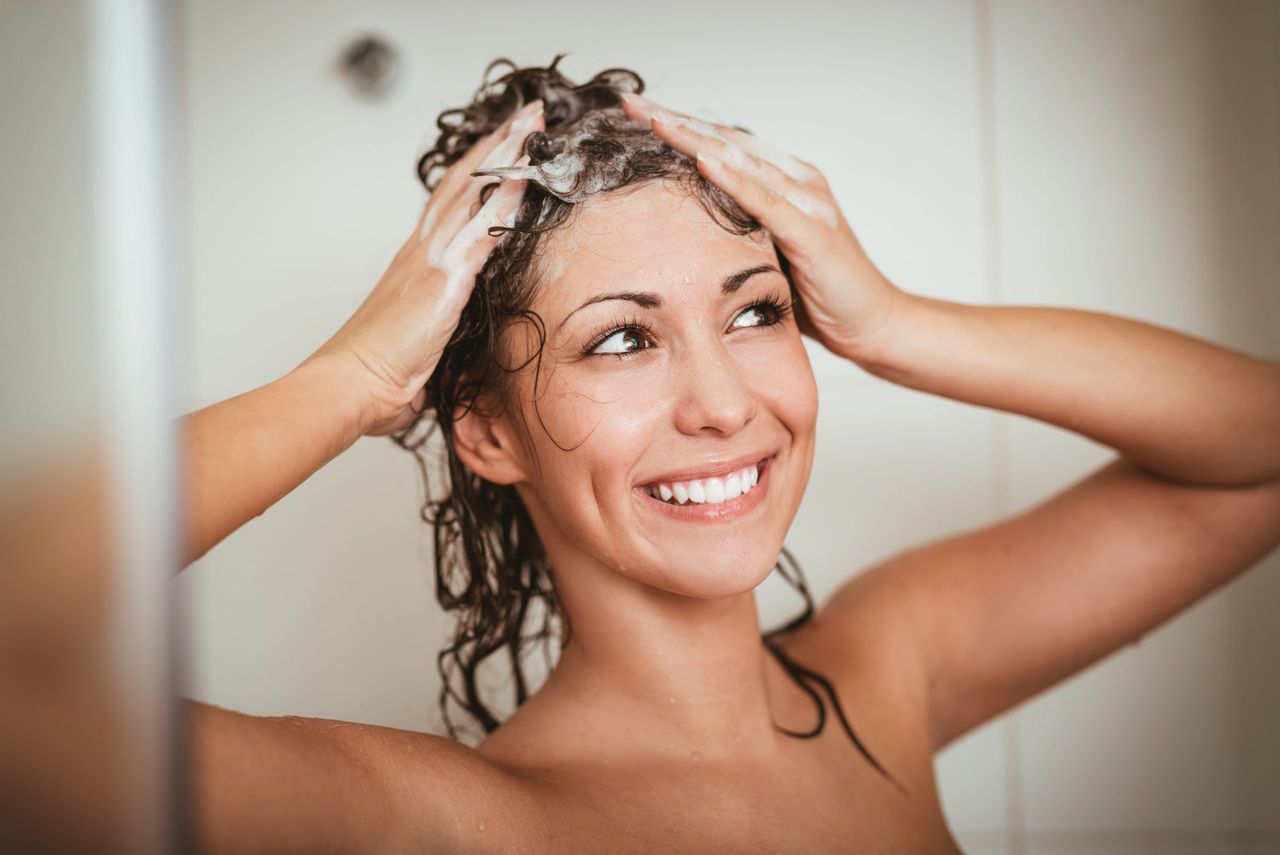 Beautiful smiling young woman washing her long hair with shampoo.
