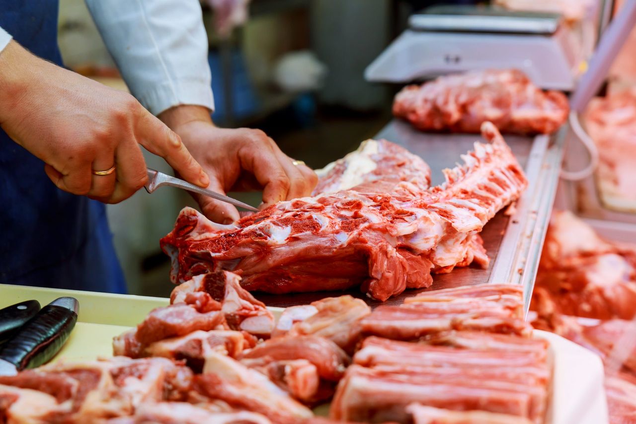 Cropped image of male butcher cutting raw meat with knife at counter in shop