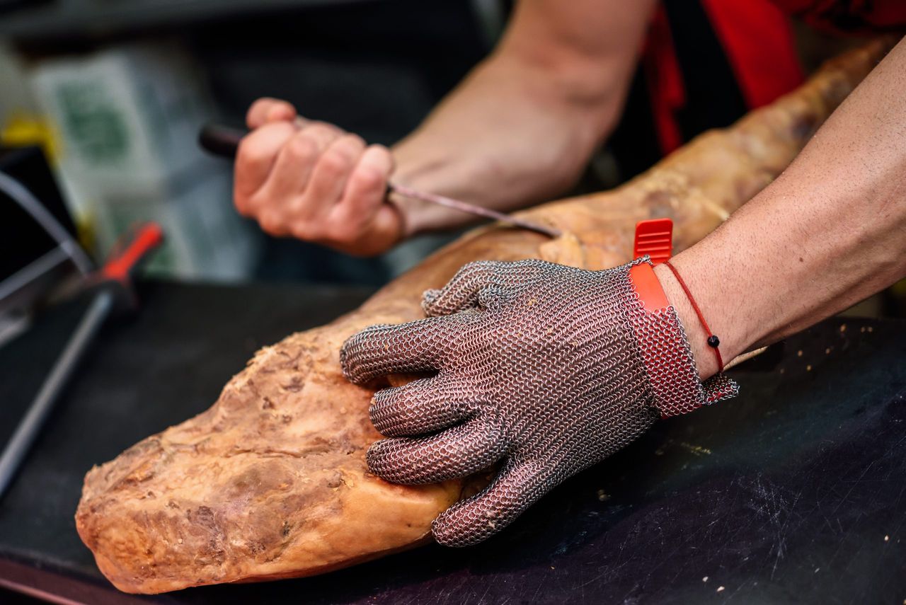 Close-up of butcher boning a ham in a modern butcher shop with metal safety mesh glove
