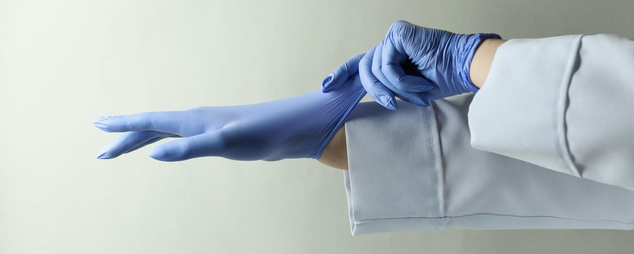 Doctor putting medical gloves on light gray background