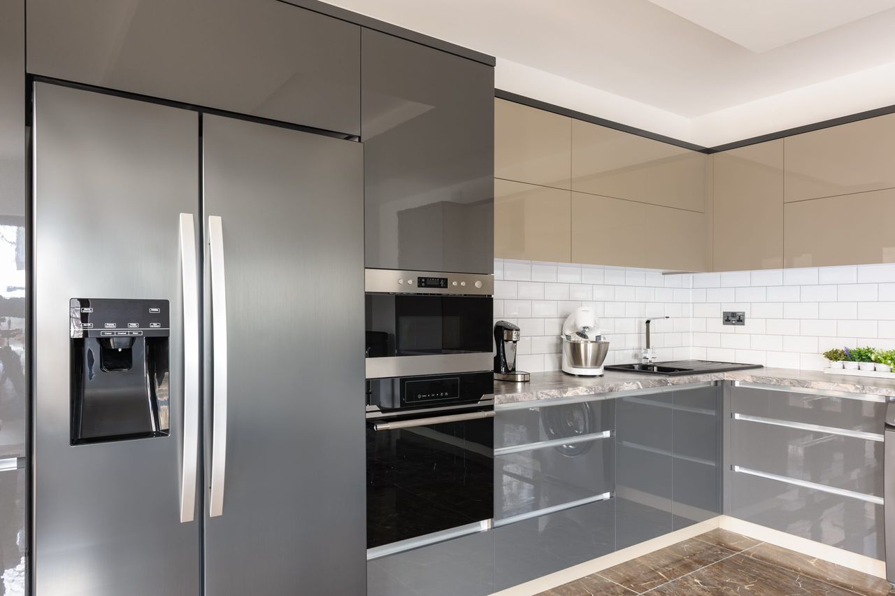 Spacious luxury well designed modern grey, beige and white kitchen withdouble sized fridge. Door of electric oven is open