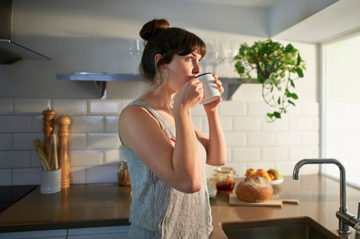 The woman is drinking coffee in the kitchen.