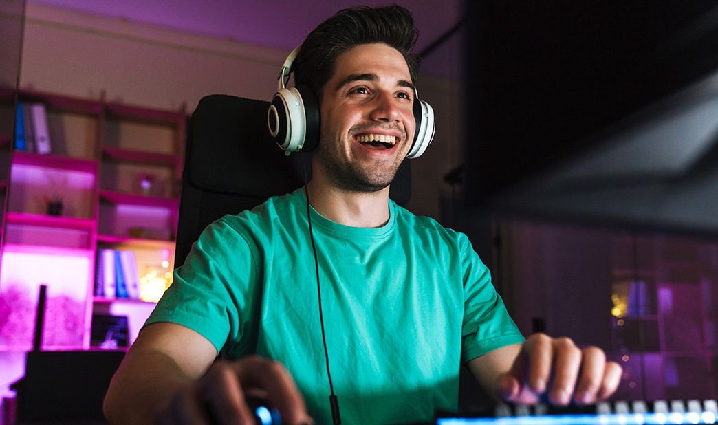 Uśmiechnięty mężczyzna w słuchawkach gra na komputerze.