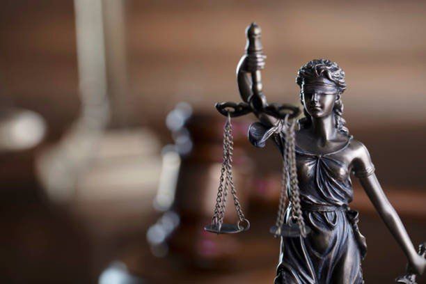 Law symbols composition: judge’s gavel, Themis sculpture and scale on the brown background.