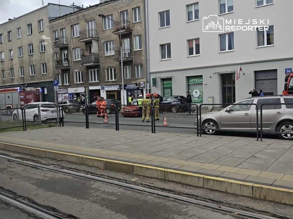 Grupa ratowników w pomarańczowych uniformach pracuje przy uszkodzonym samochodzie na ruchliwej ulicy.