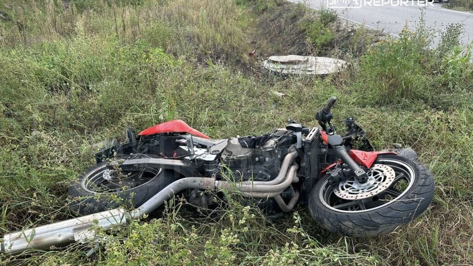Motocykl leżący na boku w wysokiej trawie przy drodze, z widocznymi uszkodzeniami.