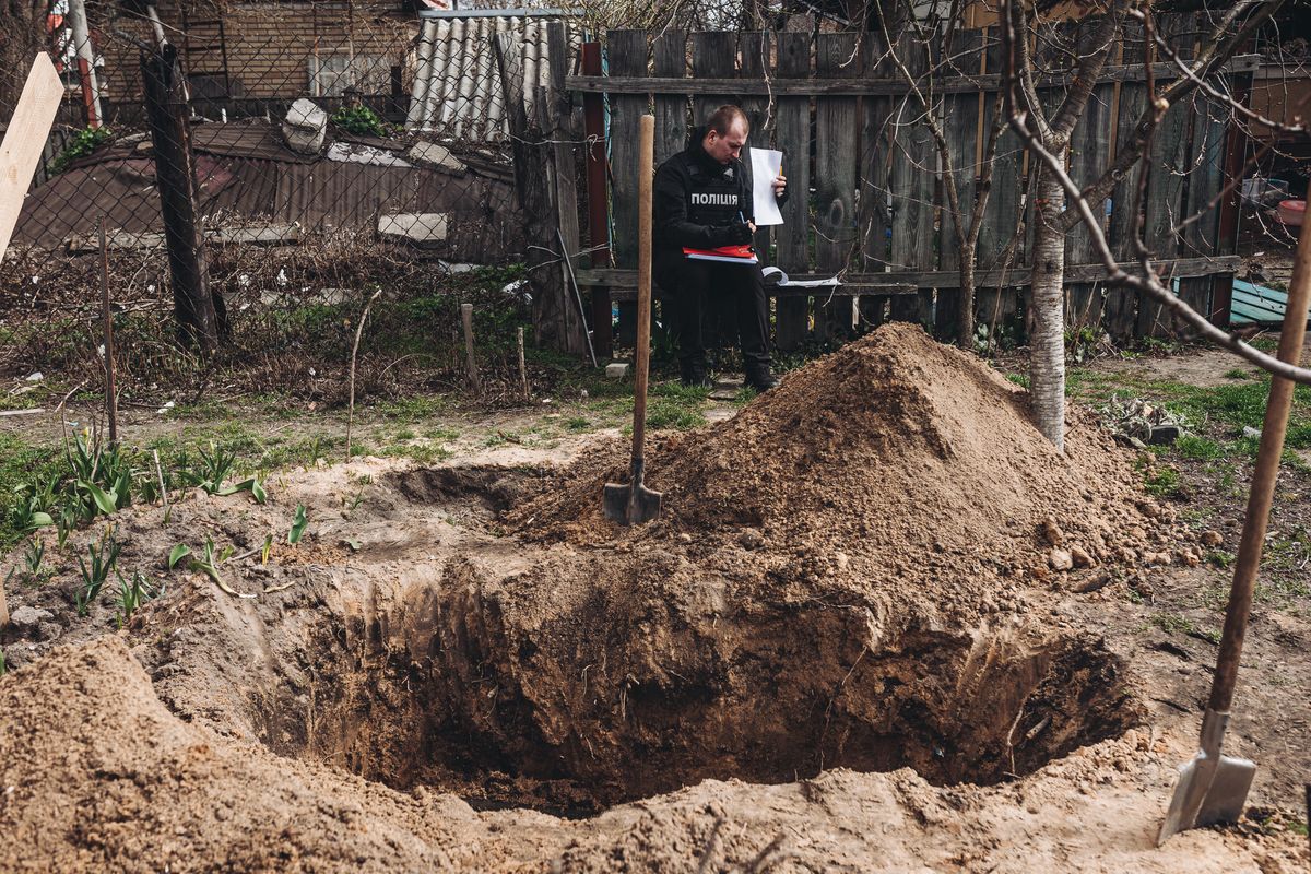 BUCHA, UKRAINE - APRIL 08: A policeman stands in front of an open grave in Bucha, Ukraine on April 08, 2022. (Photo by Diego Herrera Carcedo/Anadolu Agency via Getty Images)