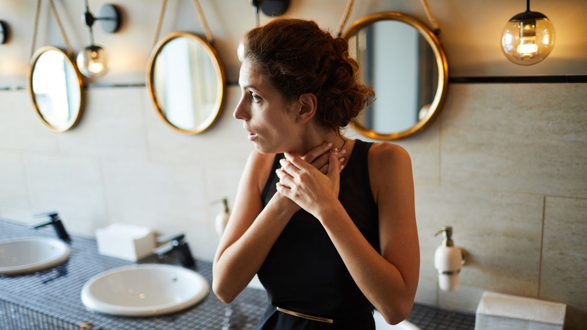 ChokingYoung brunette woman in elegant black dress touching her throat while standing in toiletPressmaster