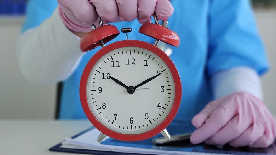 Medical professional holding red alarm clock while preparing for patient checkup