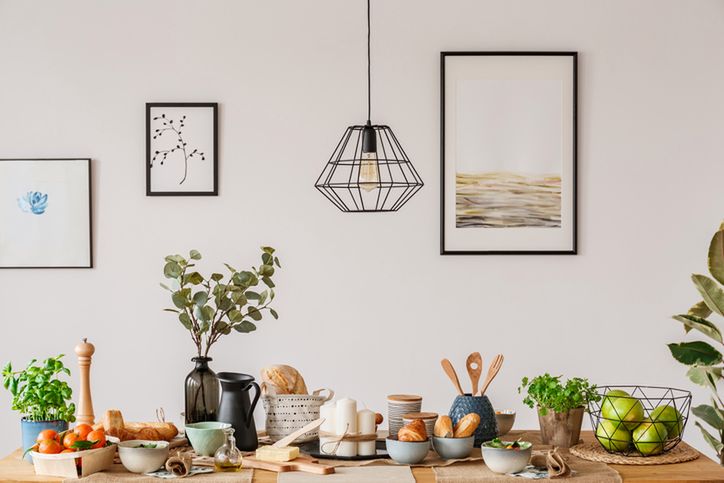 Dining room interior with white wall, art prints and a wooden table with bread and fruit 