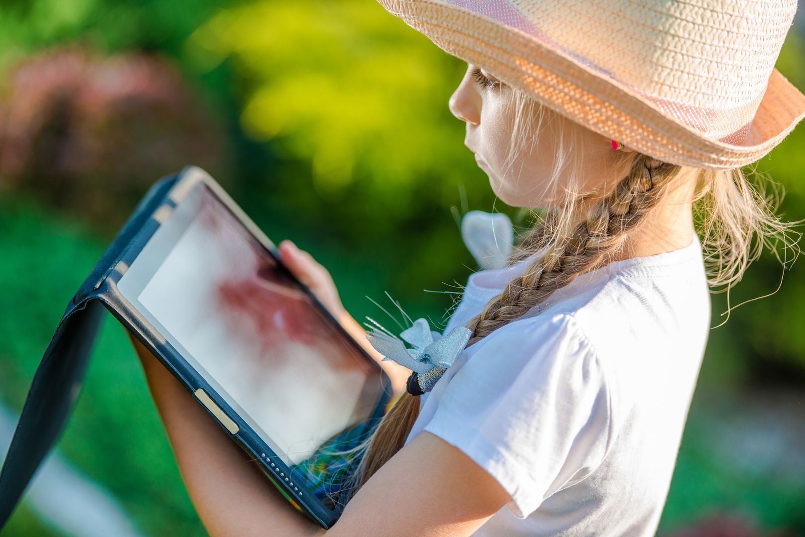 Young Caucasian Girl Playing with Tablet Device in the Garden. Closeup Photo