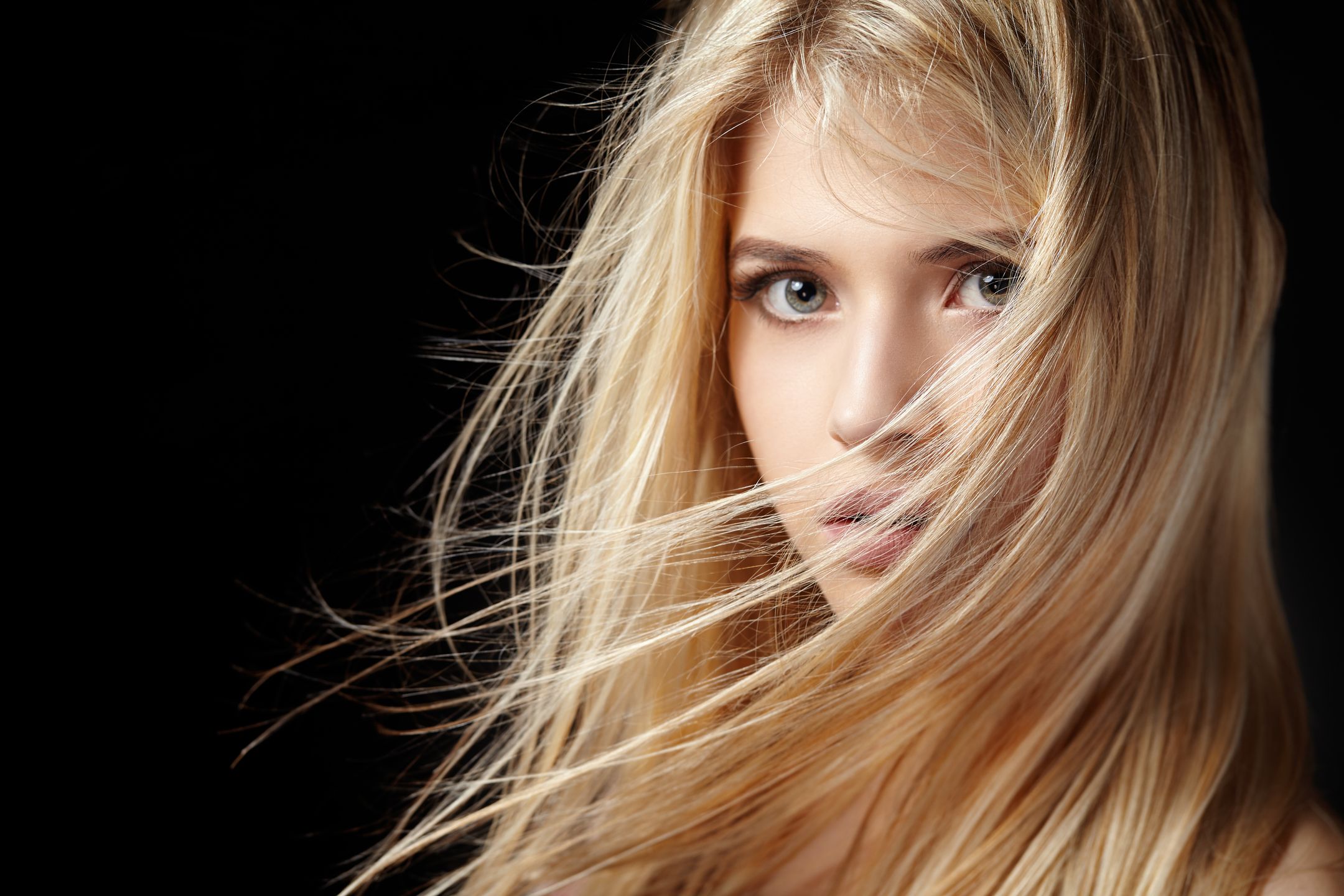 Close portrait of a beautiful young blonde woman with flying hair on a black background. 