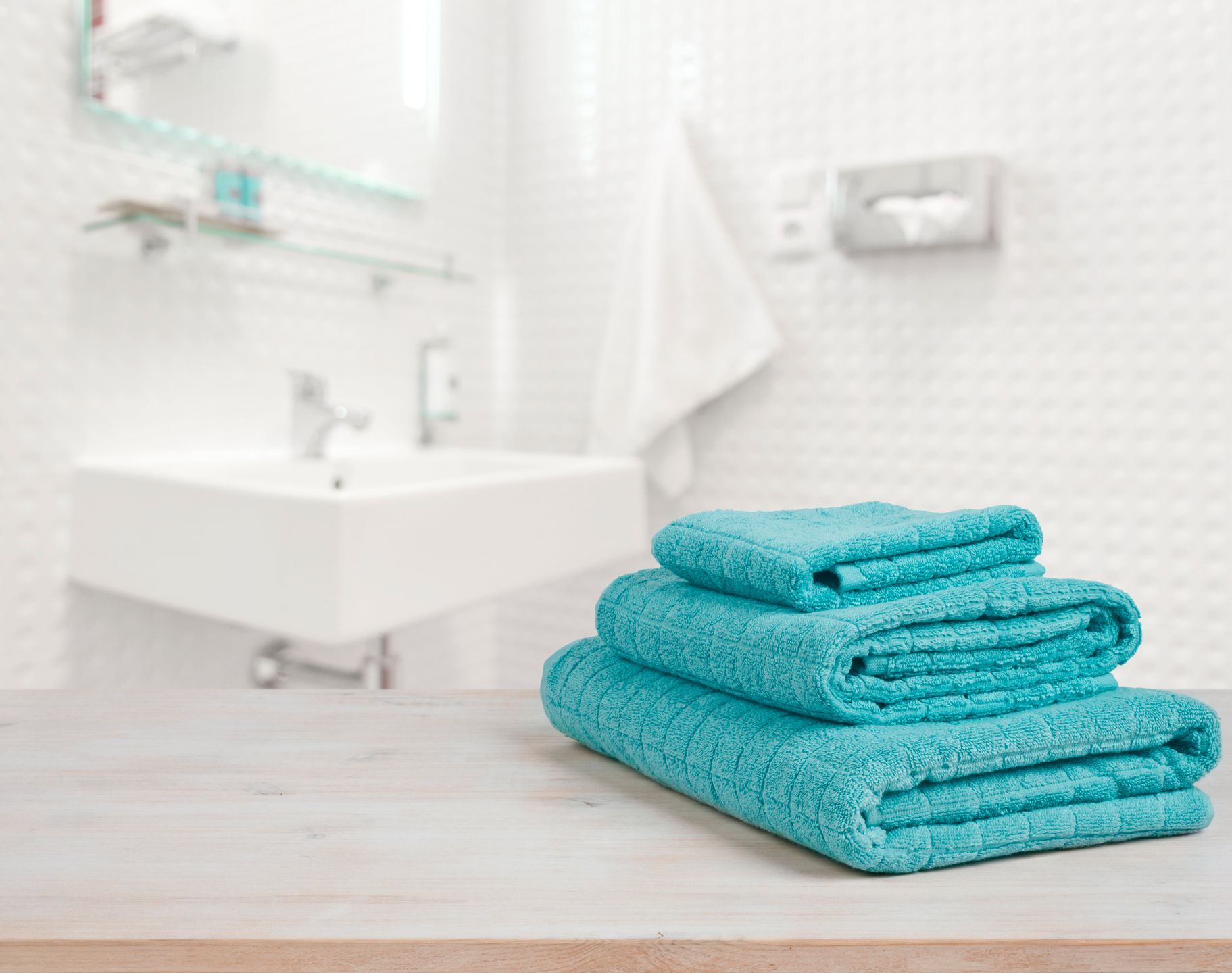 Turquoise spa towels pile on wood over blurred bathroom background 