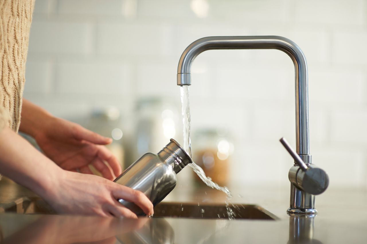 A woman cleans a plastic free and reusable water bottle in a kitchen sink, close up.