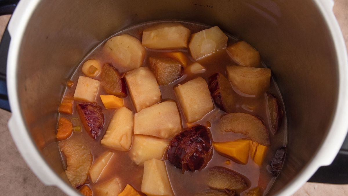 Pressure cooked vegetables, beef gravy and apple cider.Pressure cooking pan with pressure cooked ingredients which are beef gravy mixed with apple cider vinegar, chopped parsnips, black amber plums and sweet potato chops. Gravy is result of pressure cooked beef brisket in beef broth and water, together with chopped vegetables which are celery, carrots and onions as well as with spices which are nutmeg, cinnamon and allspice. Brownish surface. High point of view. Light effect.annick vanderschelden photographpressure cooking, aplle cider vinegar, black amber plums