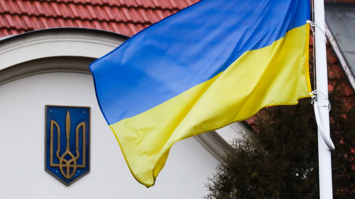 Na zdjęciu flaga Ukrainy na tle budynku z herbem tego państwa