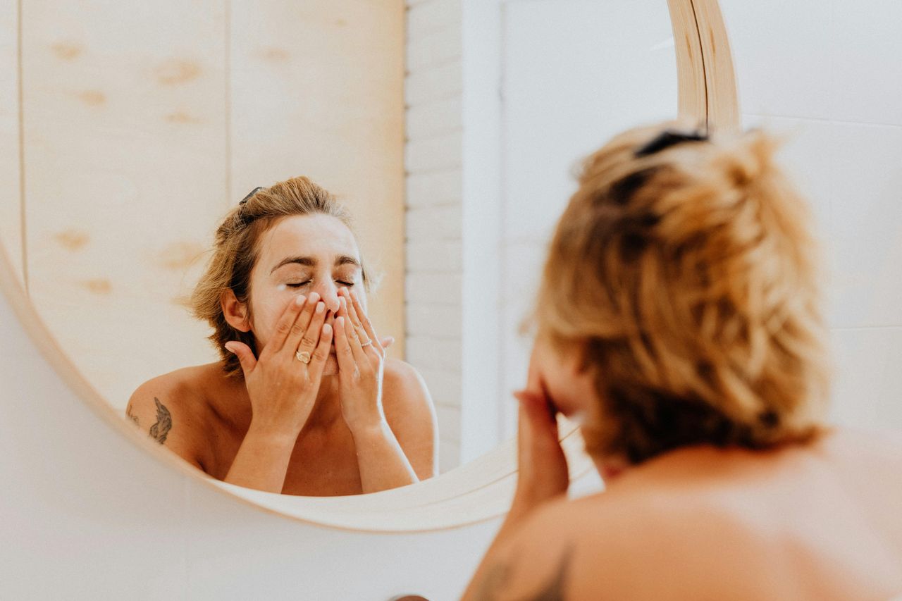 The woman washes her face in front of the mirror.