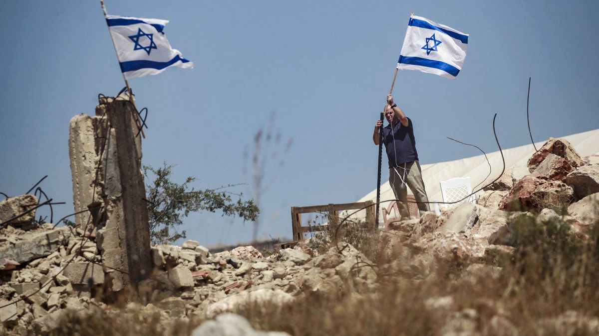 A Jewish settler raises an Israeli flag on Palestinian landSALFIT, WEST BANK, PALESTINE - 2025/05/23: A Jewish settler raises an Israeli flag on Palestinian land near Palestinian homes during an attack on the town of Bruqin, near the city of Salfit in the northern West Bank. Groups of Jewish settlers attacked and burned Palestinian homes and vehicles in the town of Bruqin, in the northern West Bank. Local residents reported that hundreds of Jewish settlers burned property, planted Israeli flags, and seized surrounding land in the town. This came after an Israeli settler was shot dead by a Palestinian near the Bruqin settlement. (Photo by Nasser Ishtayeh/SOPA Images/LightRocket via Getty Images)SOPA Imagesjewish settler, jewish, jews, illegal, attack, palestine - israeli, jewish settlers, palestine - israeli conflicts, palestinian, settlers
