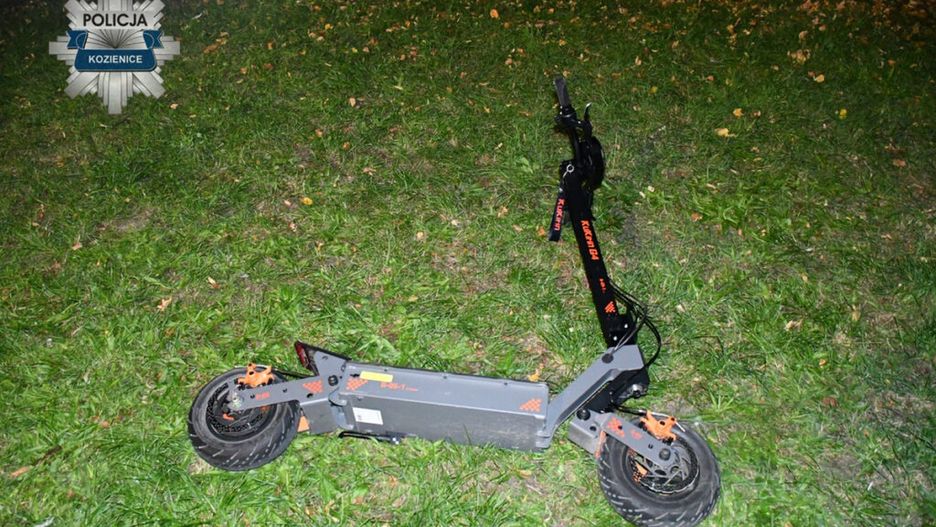 Złoty skuter elektryczny leży na trawie w nocy, obok widocznego fragmentu drogi.