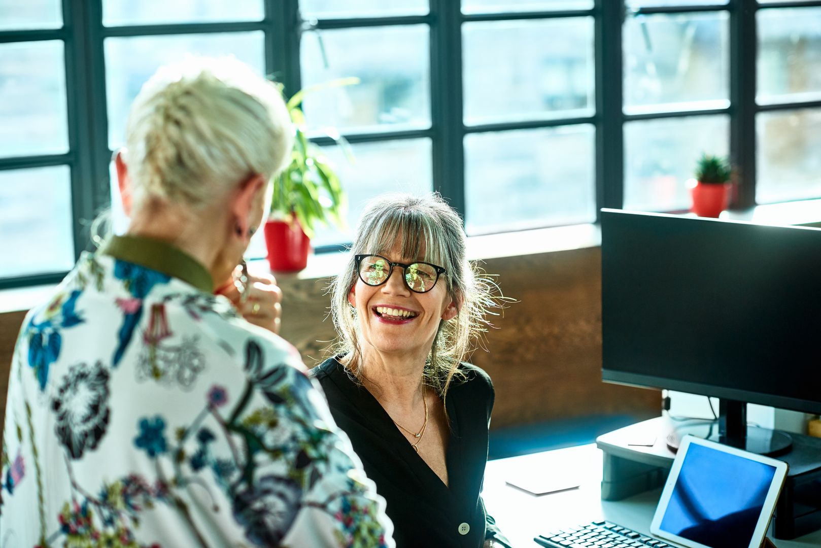 Cheerful mature woman at desk smiling towards senior female colleague
Two friends having conversation at work, woman in her 50s wearing glasses smiling and facing female manager, agreement, support, collaboration
10'000 Hours