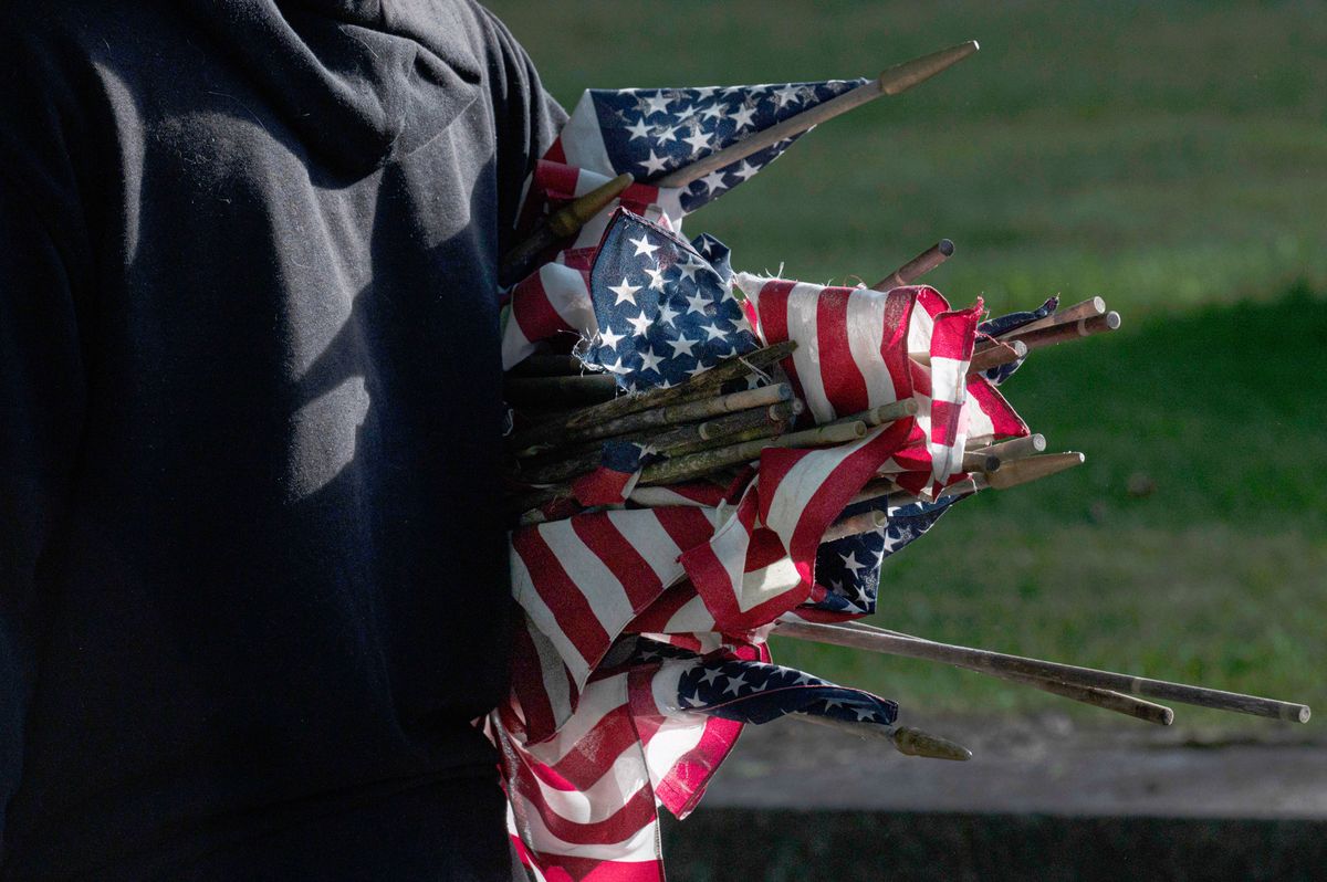 DALLAS, PENNSYLVANIA, UNITED STATES - 2022/05/25: After collecting them from the tomb, a boy carries small US flags and replaces them with new flags for the Memorial Holiday. Members of the American Legion, Boy Scouts, and Girl Scouts have been replacing tattered flags throughout cemeteries in preparation for the Memorial Day Holiday which takes place every year on May 30th. Memorial Day is observed as a federal holiday and is considered a time for remembering U.S. military personnel who died in action. (Photo by Aimee Dilger/SOPA Images/LightRocket via Getty Images)