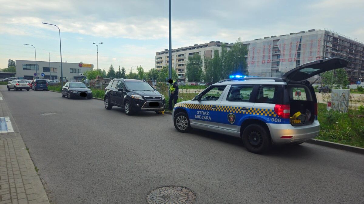 Strażnik miejski zakładający blokady na samochody na ul. Wojciechowskiej