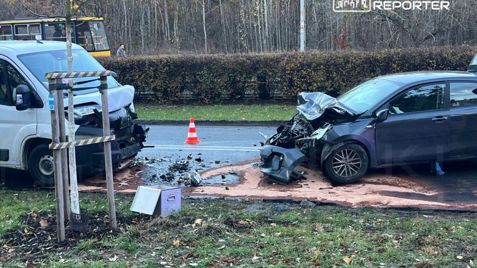 Dwa uszkodzone samochody osobowy i dostawczy z wgniecionymi przodami na poboczu drogi, obok pomarańczowy trójkąt ostrzegawczy.
