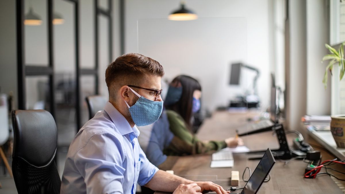 Na zdjęciu osoby w maseczkach przed komputerem pracujące w biurze