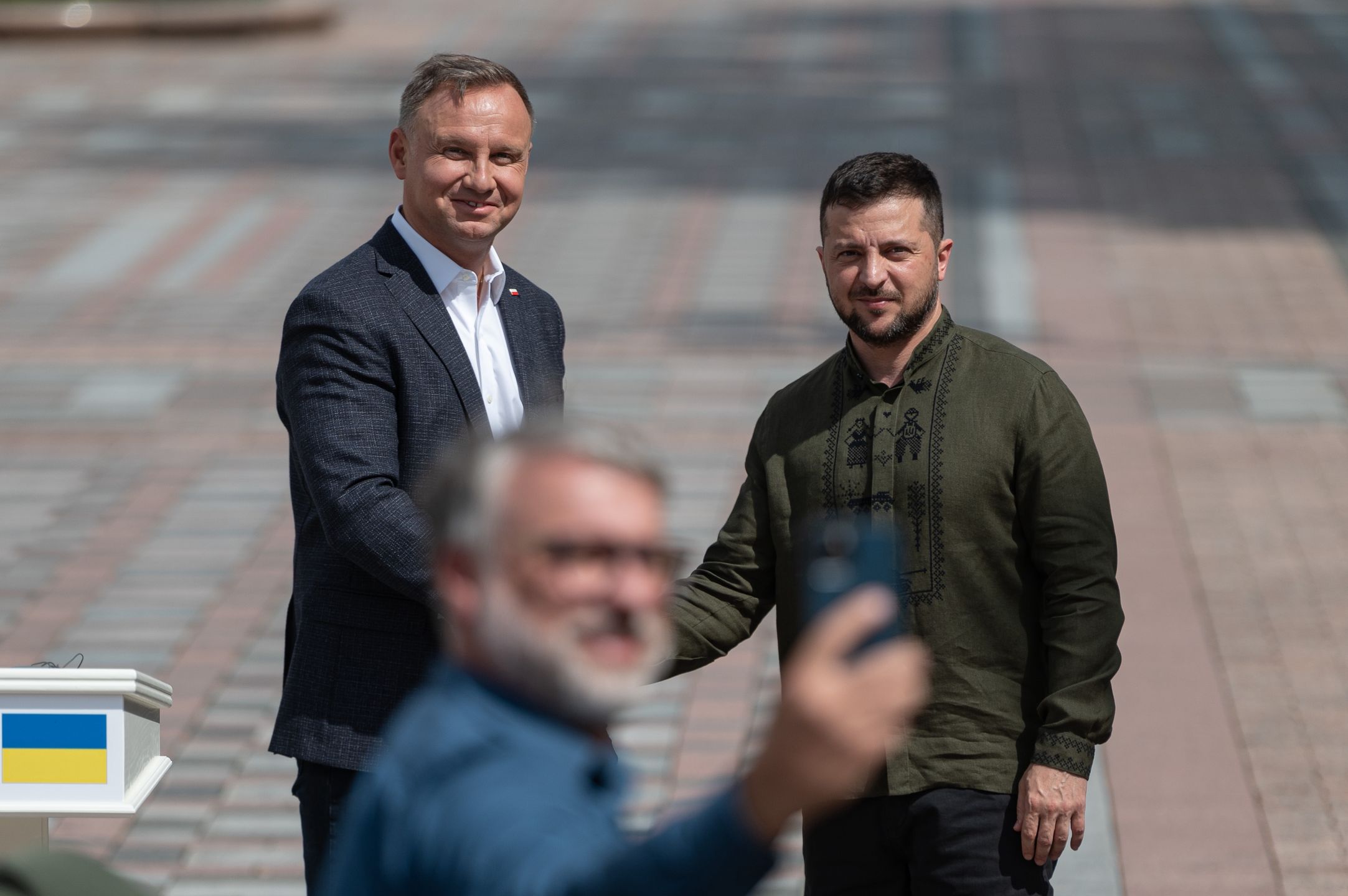 KYIV, UKRAINE - AUGUST 23: A man takes a selfie as Polish President Andrzej Duda and Ukrainian President Volodymyr Zelensky shake hands after their press conference on August 23, 2022 in Kyiv, Ukraine. Tomorrow marks six months since Russia's large-scale invasion of Ukraine, which galvanized the country's European neighbors and prompted an outpouring of political, military and economic support. (Photo by Alexey Furman/Getty Images)