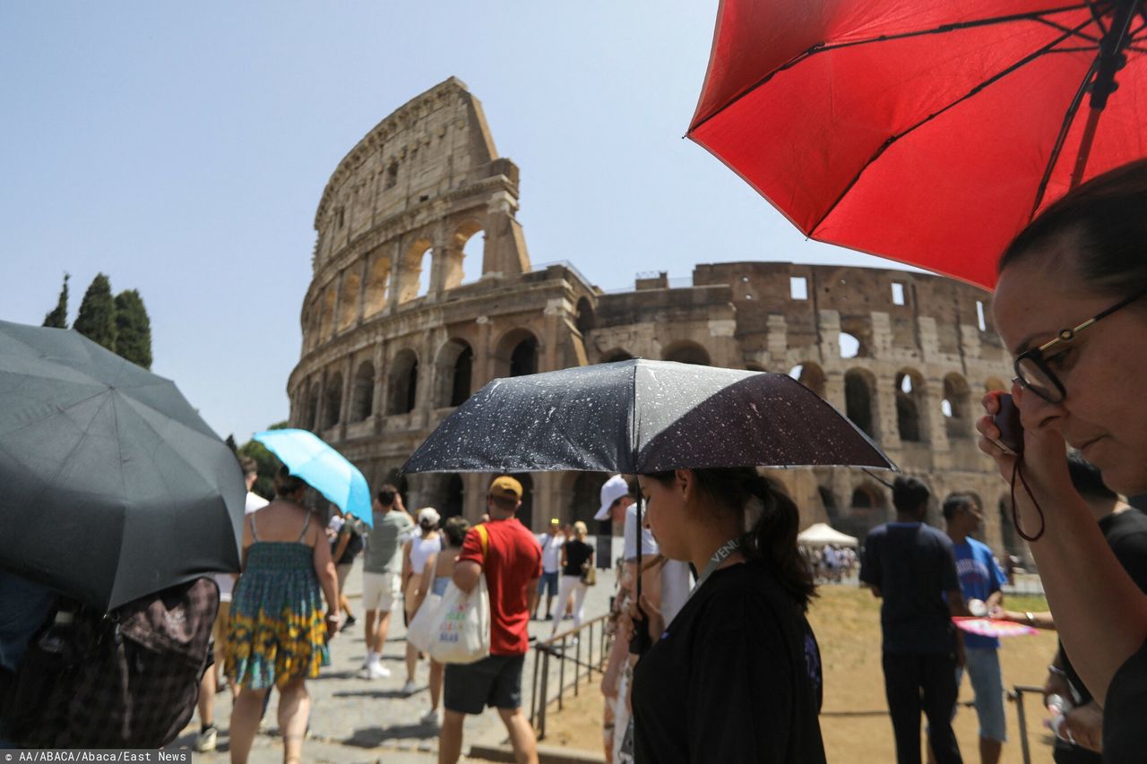 Turyści z parasolami przechodzą obok Koloseum podczas upalnego dnia w Rzymie, 18 lipca 2023 r.