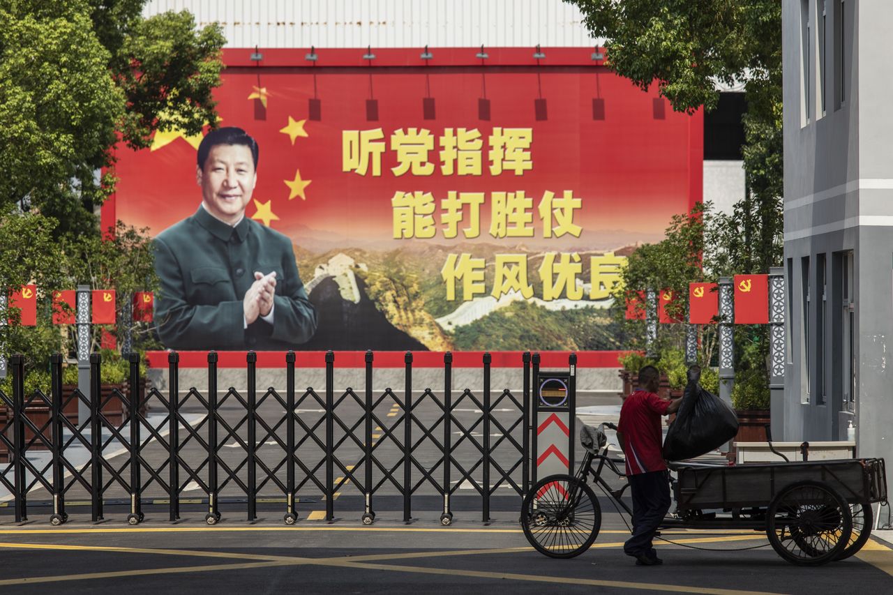 A man places a bag of trash into his rickshaw in front of a compound displaying a billboard featuring China's President Xi Jinping in Shanghai, China, on Monday, Aug. 30, 2021