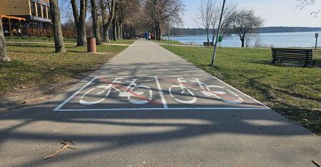 Rowerzyści lawirujący pomiędzy spacerującymi na ścieżce nad Zalewem Zemborzyckim