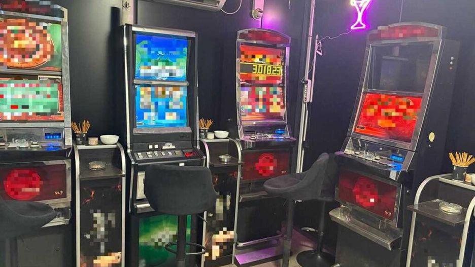 Wnętrze lokalu z automatami do gier, w którym znajdują się cztery maszyny, obok czarnych stołków barowych.