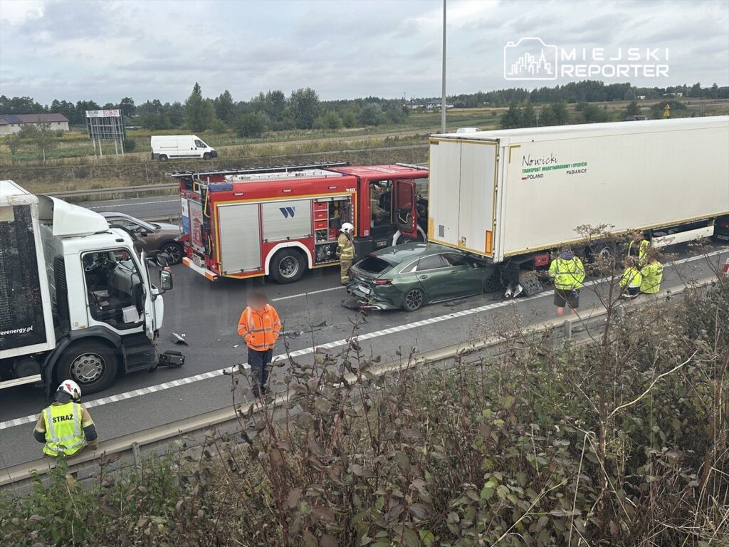 Wypadek drogowy z udziałem samochodu osobowego i ciężarówki na autostradzie, w tle straż pożarna i służby ratunkowe.