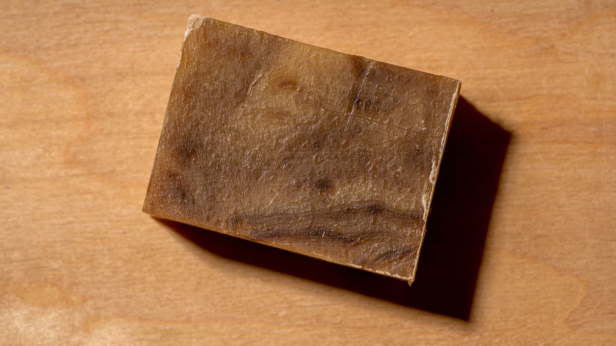 A bar of cut handmade soap on a dark brown background.A slice of cut handmade soap on a dark brown background. Tar natural cleanser for problem skin of the face and scalp care. Sustainable still lifeFiordaliso